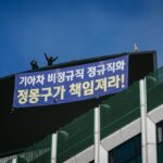 Deux travailleurs en sous-traitance chez Kia surplombent le rassemblement depuis le sommet d’un gratte-ciel à Séoul qu’ils occupent depuis juin 2015. Ils demandent au constructeur automobile de transformer les contrats d’emploi temporaires en contrats permanents. Photo: IndustriALL/Jun Michael Park 
